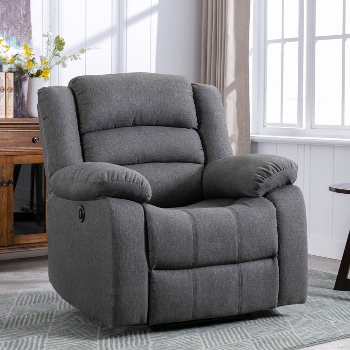 A gray, plush recliner chair with padded armrests and a tufted backrest, situated in a well-lit room with a wooden cabinet and window in the background.