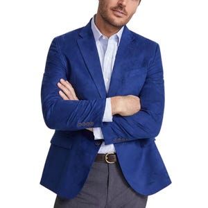 A man is wearing a Nautica Faux-Suede Sport Coat in a vibrant blue color, paired with a light blue checkered shirt and gray pants. The coat features button cuffs and a notched lapel.