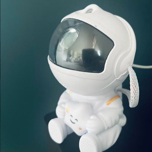 A small astronaut shaped projector sitting on a black counter in front of a dark teal background.
