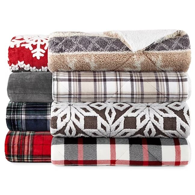 A stack of various patterned plush blankets, including plaid and snowflake designs.