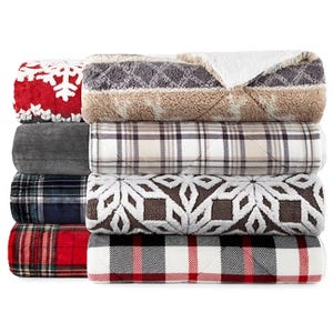 A stack of various patterned plush blankets, including plaid and snowflake designs.