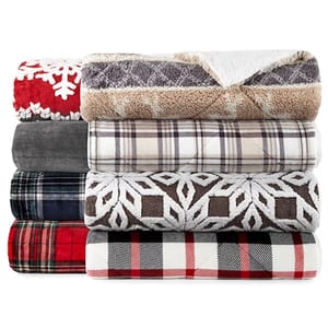 A stack of various patterned plush blankets, including plaid and snowflake designs.