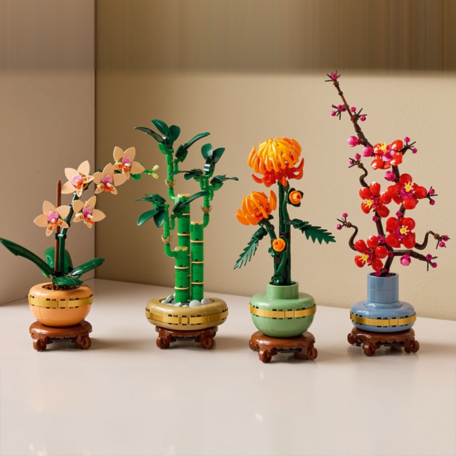 Four LEGO botanical sets featuring a variety of plants: an orchid, bamboo, an orange chrysanthemum, and cherry blossoms, each displayed in decorative pots.