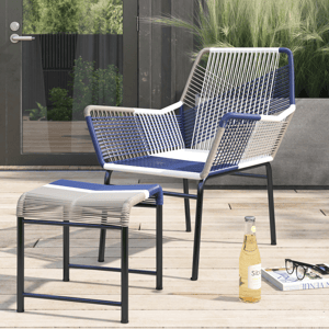A modern outdoor chair and ottoman set featuring a woven rattan design with blue, white, and gray tones on a black metal frame. They are placed on a wooden deck alongside a bottle of drink, glasses, and a magazine.