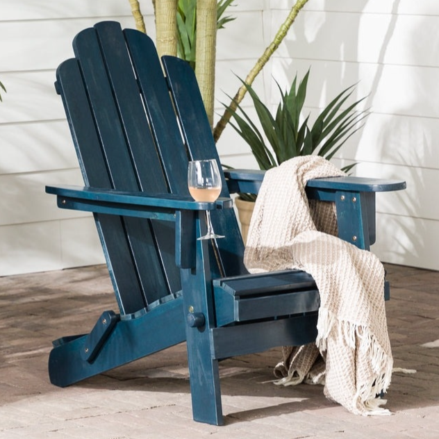 A blue Adirondack chair with a glass of wine and a beige blanket is placed on a patio surrounded by tropical plants.