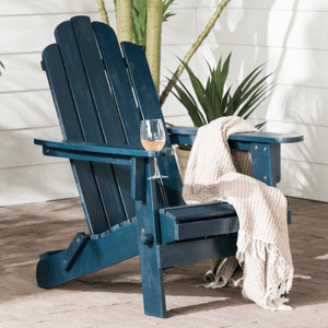 A blue Adirondack chair with a glass of wine and a beige blanket is placed on a patio surrounded by tropical plants.