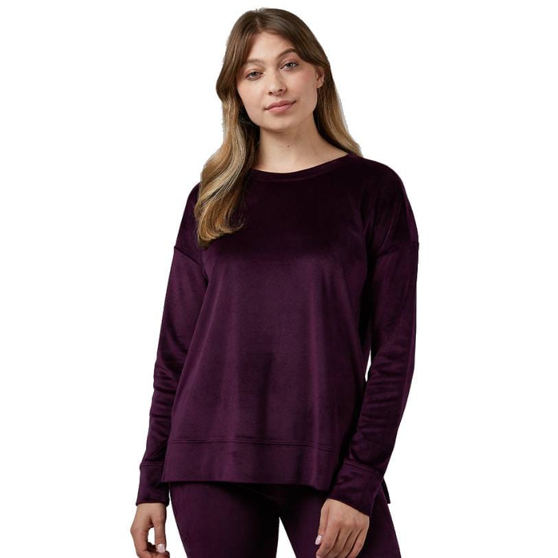 A woman is wearing a long-sleeve, rich purple velour crew top with a relaxed fit and a dropped shoulder design.