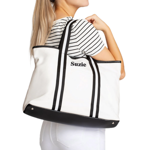 White canvas tote bag with black stripes and the name \“Suzie\“ embroidered on the front. It has black handles and a black base, worn by a person in a striped shirt.