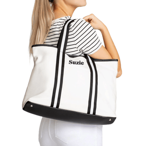 White canvas tote bag with black stripes and the name \“Suzie\“ embroidered on the front. It has black handles and a black base, worn by a person in a striped shirt.