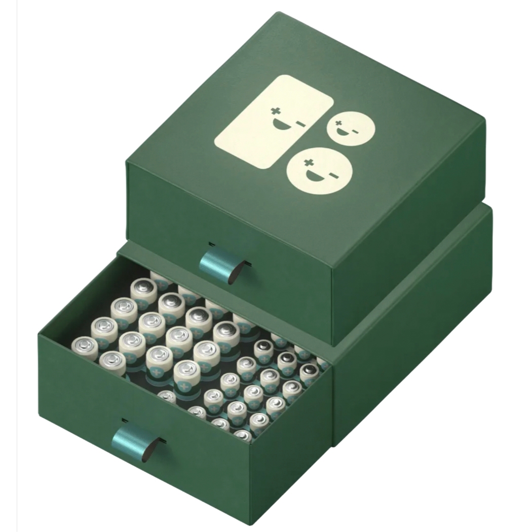 A green storage box with handles, featuring a design of smiling battery icons, contains various battery sizes neatly organized in two drawers.