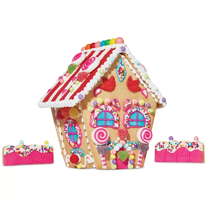 Macy's DIY Holiday House Cookie Kit includes a gingerbread house decorated with colorful candy, icing details, and two pink rectangular cookies with sprinkles. The set is vibrant, featuring lollipops, jelly beans, and a variety of sweets for decoration.