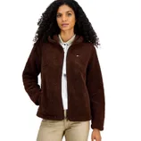 A woman is wearing a brown fleece jacket with a small logo on the chest, paired with beige pants and a light-colored collared shirt.