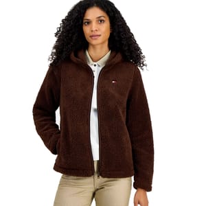 A woman is wearing a brown fleece jacket with a small logo on the chest, paired with beige pants and a light-colored collared shirt.