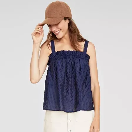 Woman wearing a navy blue ruffled tank top and a brown baseball cap.