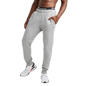 Gray fleece joggers with an elastic waistband featuring the Champion logo and a small Champion emblem on the left thigh, paired with white sneakers.