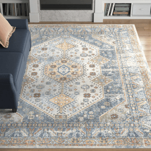 A machine-washable area rug measuring 8' x 10' features a geometric pattern with hexagonal shapes and floral motifs, primarily in blue, beige, and yellow tones, placed on a hardwood floor next to a navy couch.