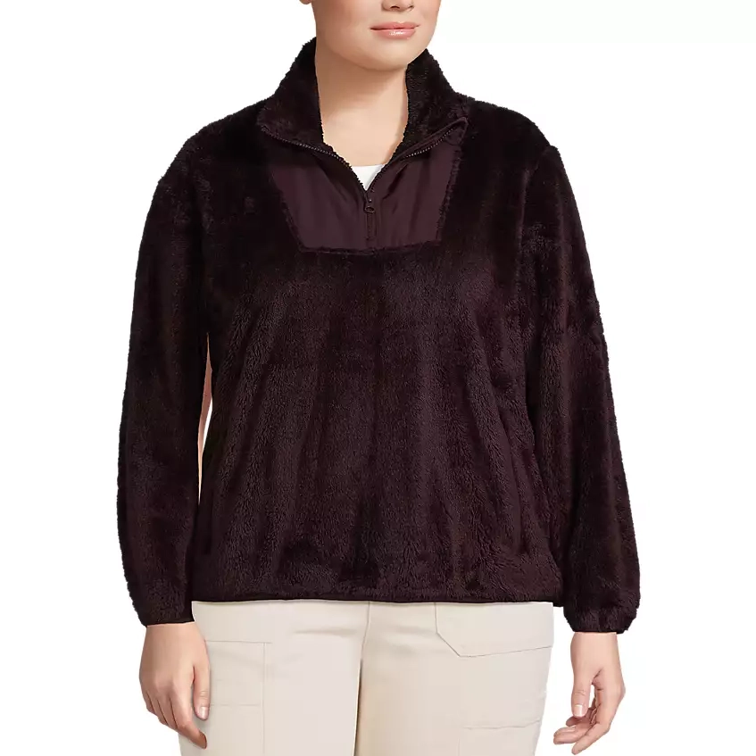 A woman is wearing a dark brown faux fur pullover with a quarter-zip design. She is also wearing light-colored pants.