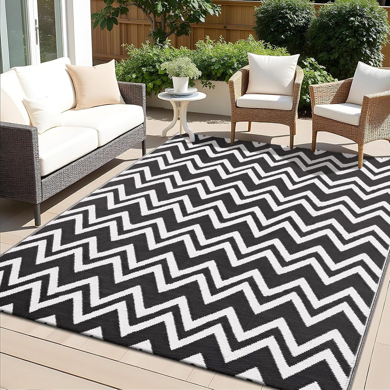 Black and white chevron-patterned outdoor rug, measuring 5' x 8', placed on a patio with a wicker sofa and chairs, surrounded by greenery.