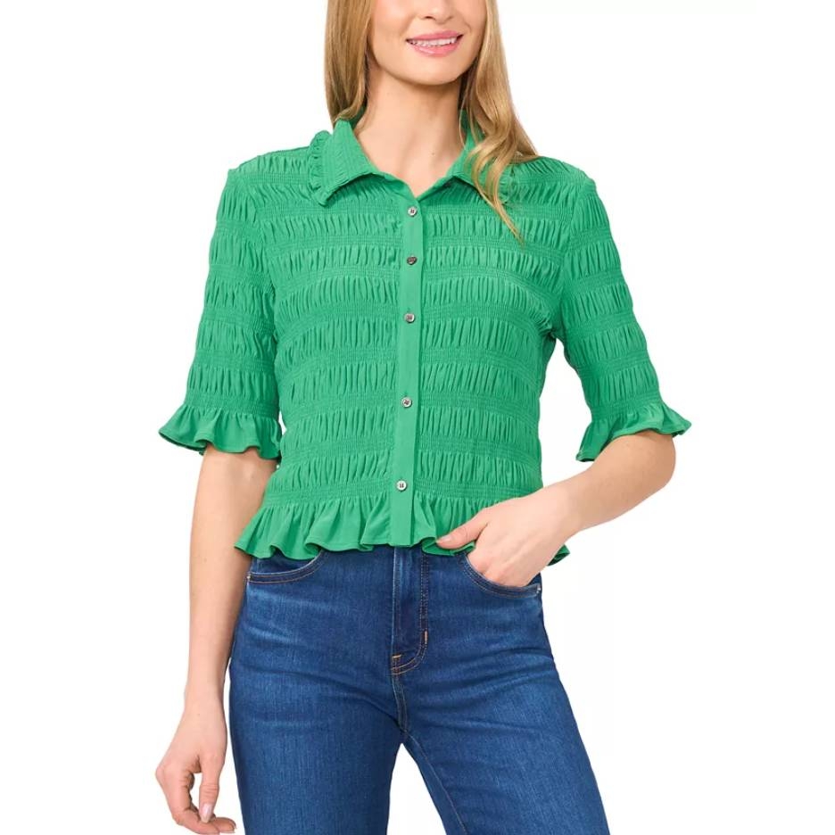 A woman is wearing a green, textured button-up blouse with ruffled sleeves and hem, paired with blue jeans.