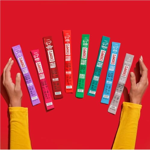 A variety of Chomps beef sticks in different colorful packaging are displayed on a red background, each labeled with \“100% Grass Fed Beef\“ and \“Zero Sugar.\“ Hands in yellow sleeves frame the arrangement.