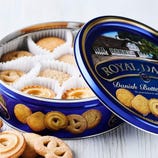 Blue tin of Royal Dansk Danish Butter Cookies, featuring an assortment of cookies in white paper cups with a variety of shapes like pretzels and swirls. The lid shows an image of a house and emphasizes no preservatives or colors are added.