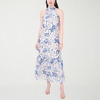 A woman is wearing a halter neck maxi dress with a blue and white floral pattern, paired with beige heeled sandals.