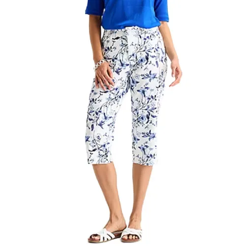 Woman wearing floral capri pants and a blue top with white sandals.