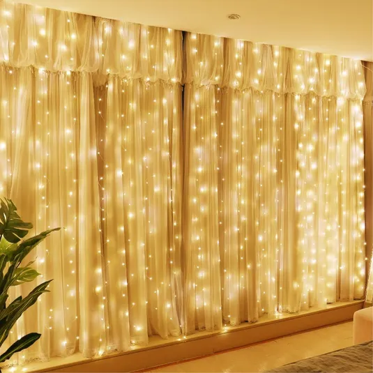 Warm white LED string lights draped over sheer curtains create a cozy, illuminated backdrop. A plant is partially visible on the left.