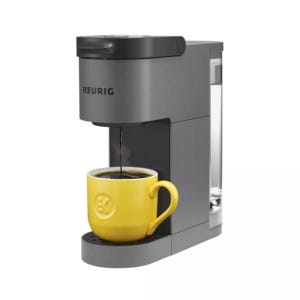 A Keurig coffee maker in gray is brewing coffee into a yellow mug.