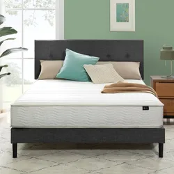 A neatly made bed with a minimalistic white mattress featuring a wave pattern, placed on a dark upholstered bed frame. The setting includes neutral and teal pillows and a wooden nightstand with a lamp.