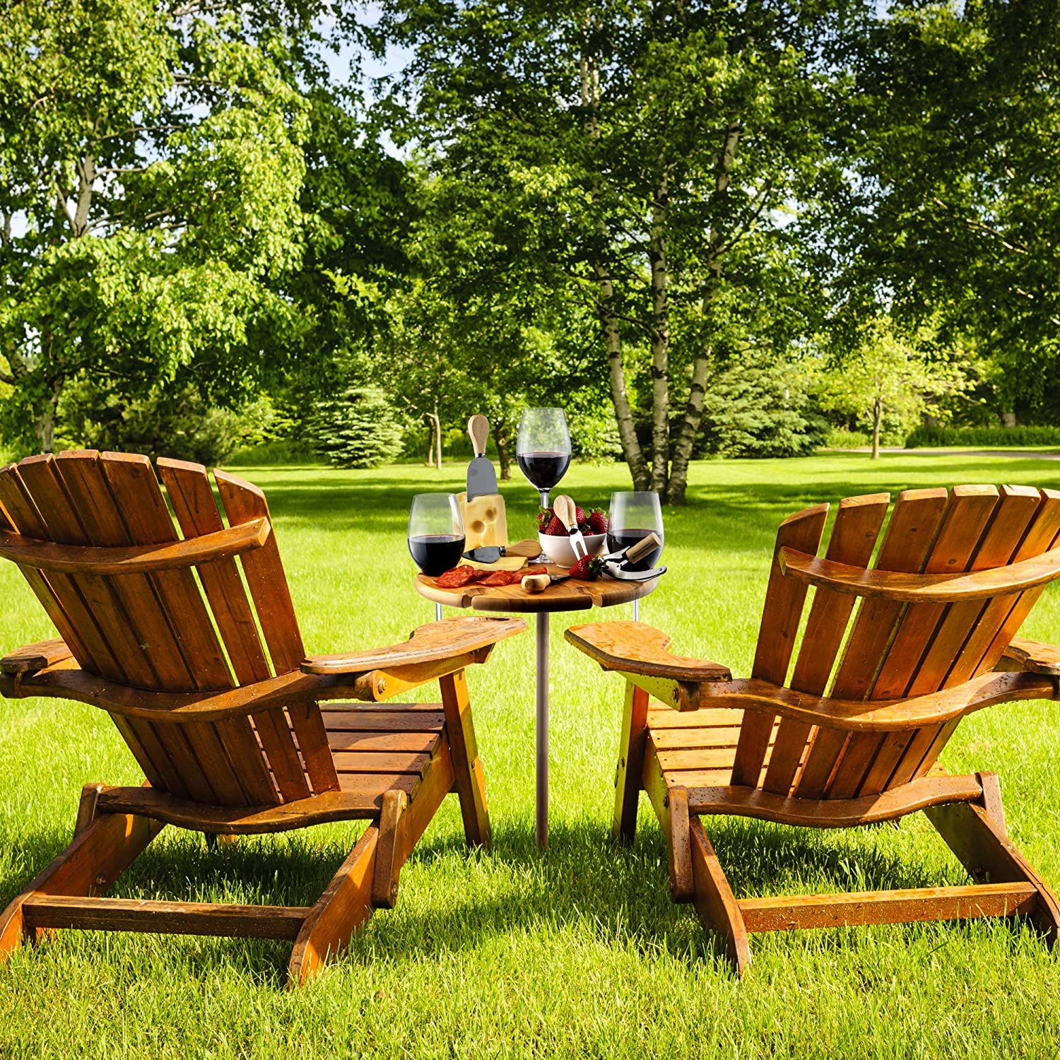 Two wooden Adirondack chairs facing each other with a small table holding wine, glasses, and snacks between them, set on a grassy lawn.