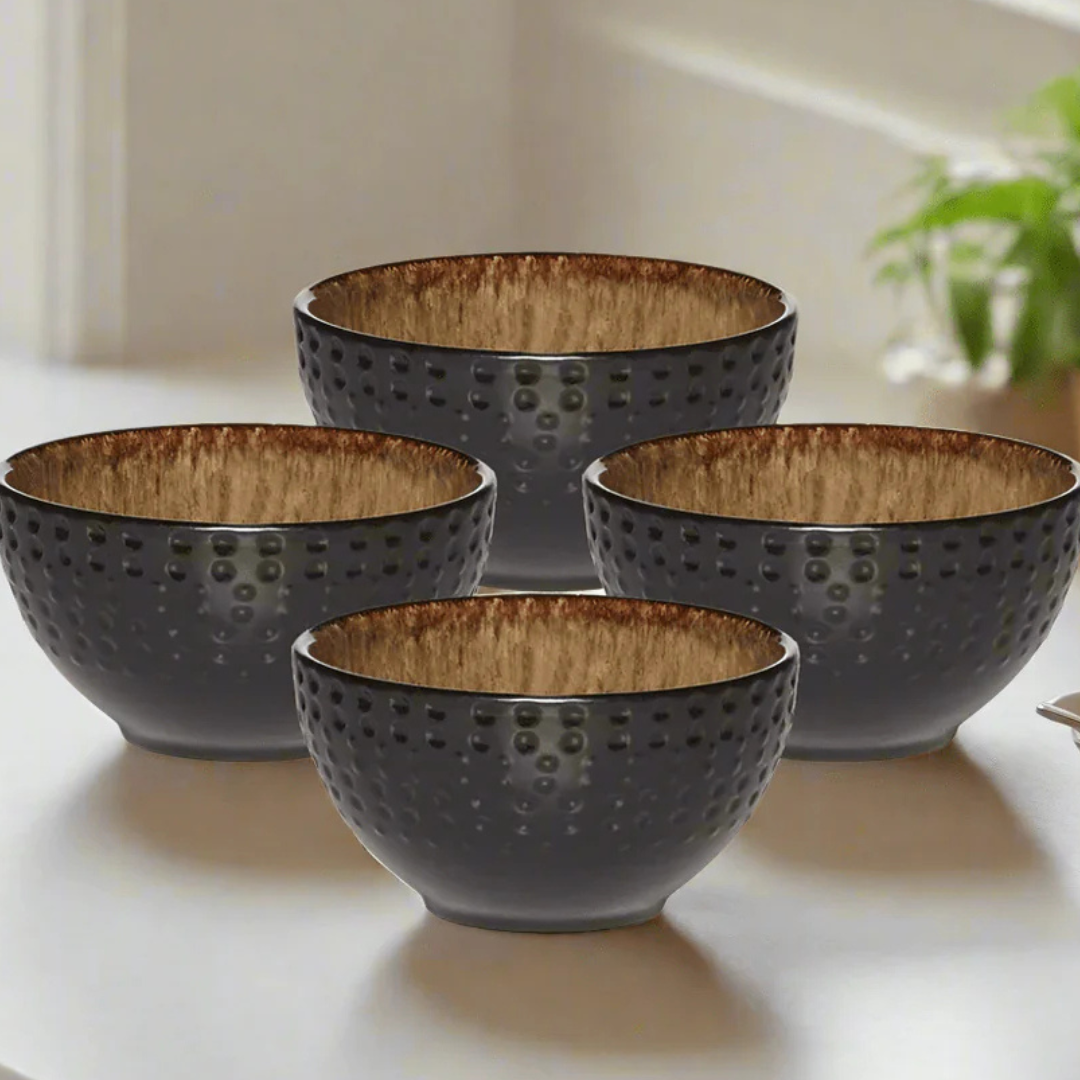 Four textured black bowls with a warm brown interior are arranged on a white surface, showing a decorative and functional design.