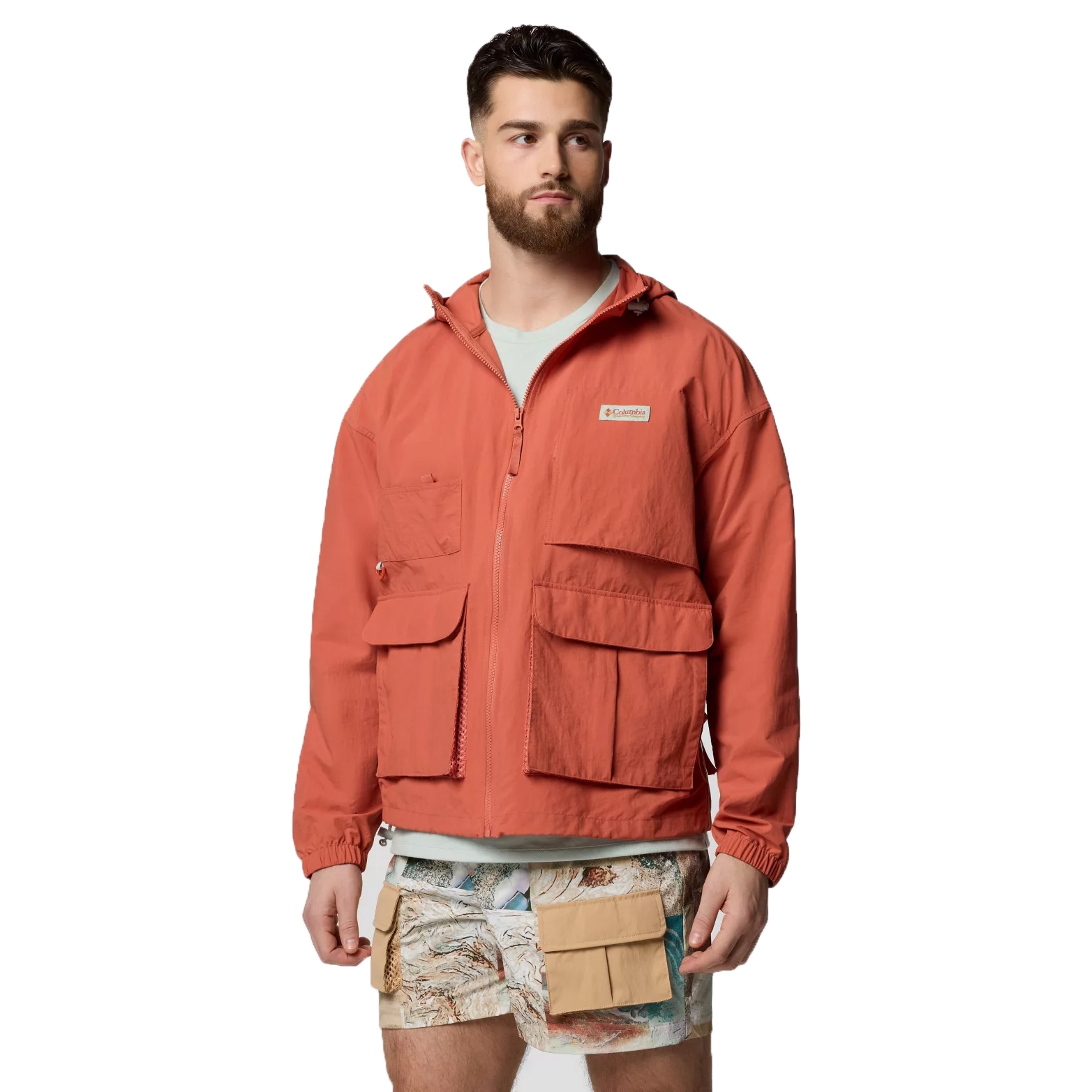 A man models an orange Columbia jacket with multiple pockets, paired with map-patterned shorts featuring additional beige pockets.