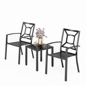 Two black metal chairs with geometric back designs are placed beside a matching table. A gold vase with pink flowers is set on the table.