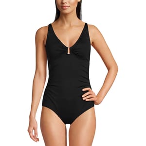 A woman is wearing a black one-piece swimsuit with a V-neckline and ruched detailing at the bust.