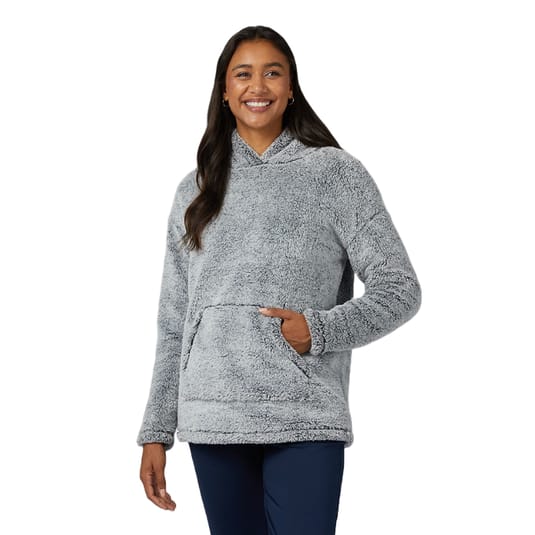 A woman is wearing a light gray, long-sleeve Sherpa pullover with a hood and a front kangaroo pocket, paired with navy blue pants. The pullover has a soft, plush texture ideal for warmth and comfort.
