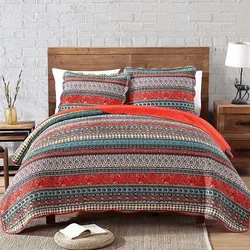 A patterned bedding set with red and turquoise colors, including a comforter and two pillowcases on a wooden bed frame.