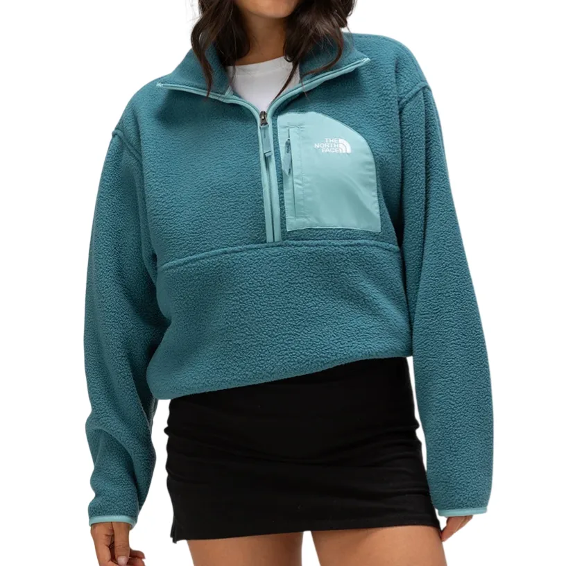 A woman wears a teal fleece pullover with a front pocket from The North Face, paired with a black skirt.