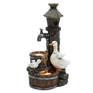 A decorative outdoor fountain featuring a rustic birdhouse with a thatched roof and LED-lit water flowing from a spout into wooden barrels, accompanied by a mother duck and two ducklings.