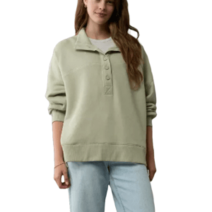 A woman is wearing a light green Henley sweater from American Eagle, featuring a buttoned neckline, long sleeves, and a relaxed fit. It is paired with light blue jeans.