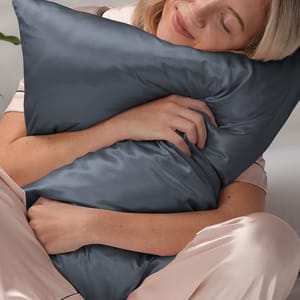 A person is hugging a dark gray silk pillow while wearing light pink satin pajamas.
