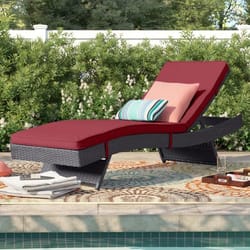 A rattan outdoor chaise lounge with red cushions is positioned by a pool, accompanied by decorative throw pillows in striped and solid patterns, and a colorful outdoor rug.