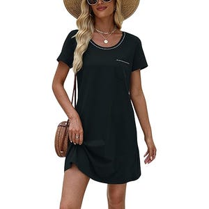 A woman wearing a black short-sleeve dress with pocket details and a wide-brimmed straw hat, accessorized with sunglasses, necklaces, and a round wicker handbag.