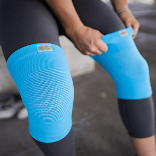 A person is wearing bright blue knee sleeves over black leggings. These sleeves are likely designed for support or compression during physical activities.