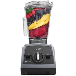 A Vitamix blender with a digital timer display is filled with various fruits, including raspberries, blackberries, mango slices, and beetroot slices.