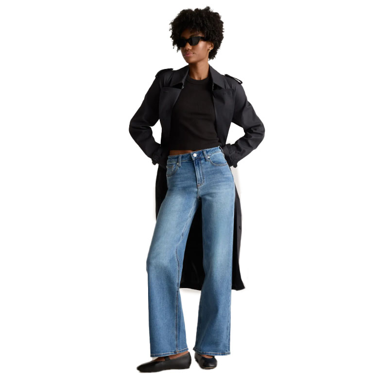 A person is wearing a black trench coat, black top, blue wide-leg jeans, black shoes, and sunglasses.