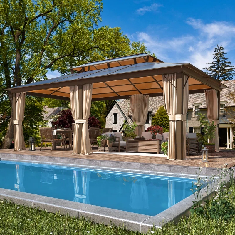 A spacious pergola with a beige canopy and sheer curtains stands on a wooden deck beside a swimming pool, complemented by outdoor furniture and greenery.
