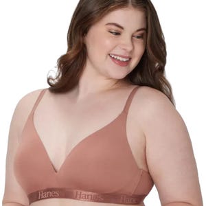 A woman is wearing a Hanes branded bra in a nude color, featuring a seamless, wire-free design with adjustable straps.