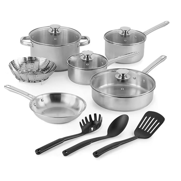 The 13-piece JCPenney Cookware Set includes stainless steel pots and pans with lids, a skillet, a saucepan, a sauté pan, a steamer insert, and three black plastic utensils – a pasta fork, a serving spoon, and a slotted spatula.