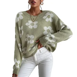 A light green oversized sweater with white floral patterns is paired with white pants. The outfit is accessorized with large hoop earrings and layered necklaces.